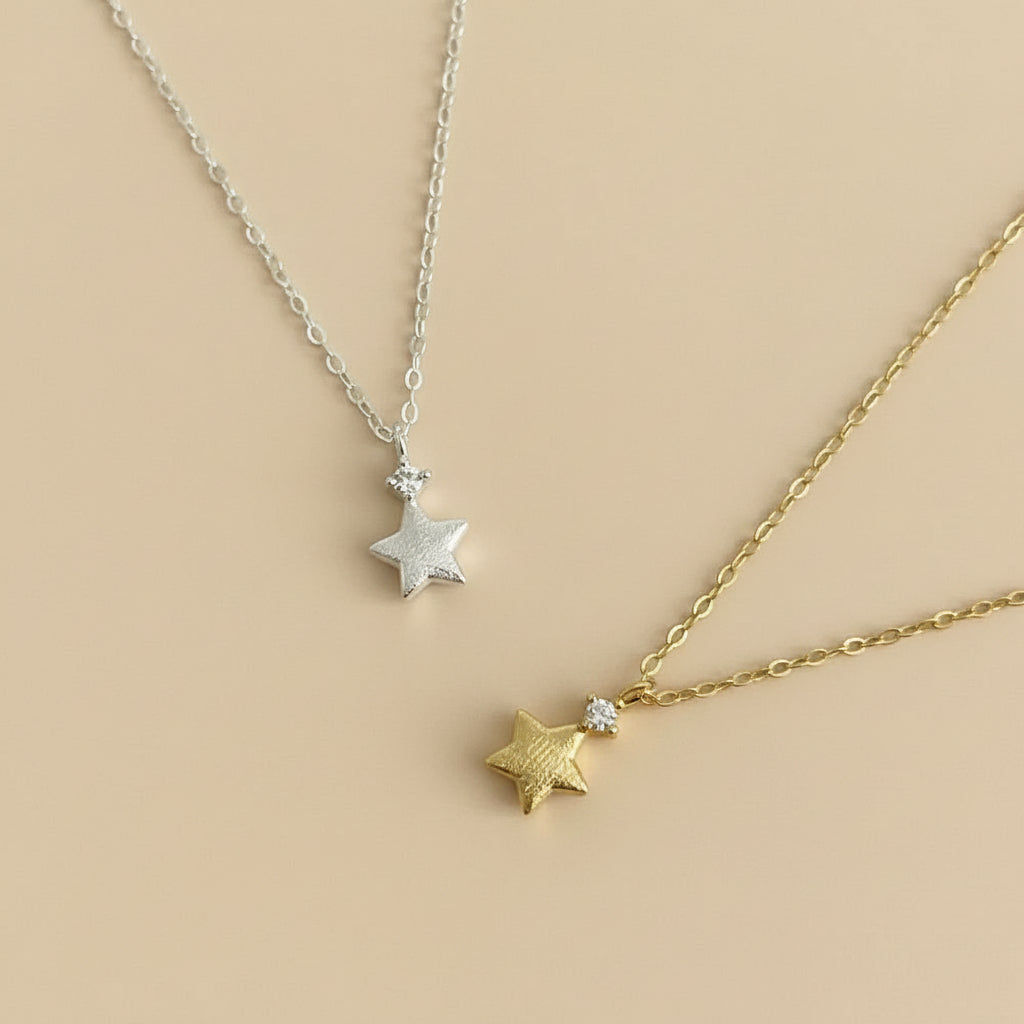 Two star-shaped necklaces, one gold and one silver, on a beige surface.