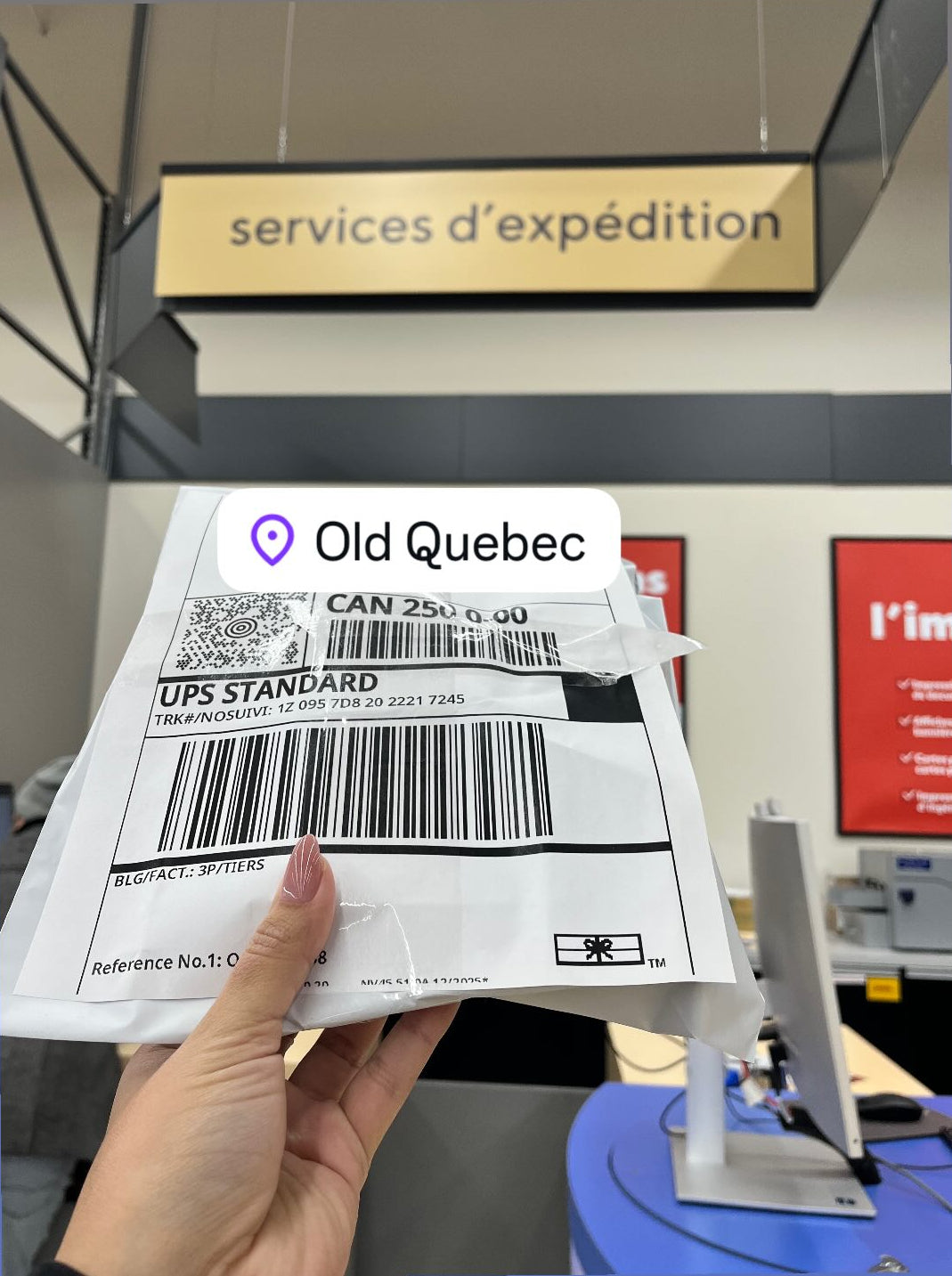 Hand holding a UPS shipping label with 'Old Quebec' branding in an office setting.
