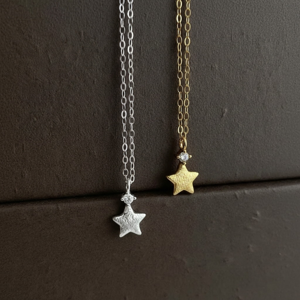Two star-shaped necklaces, one silver and one gold, on a dark surface.