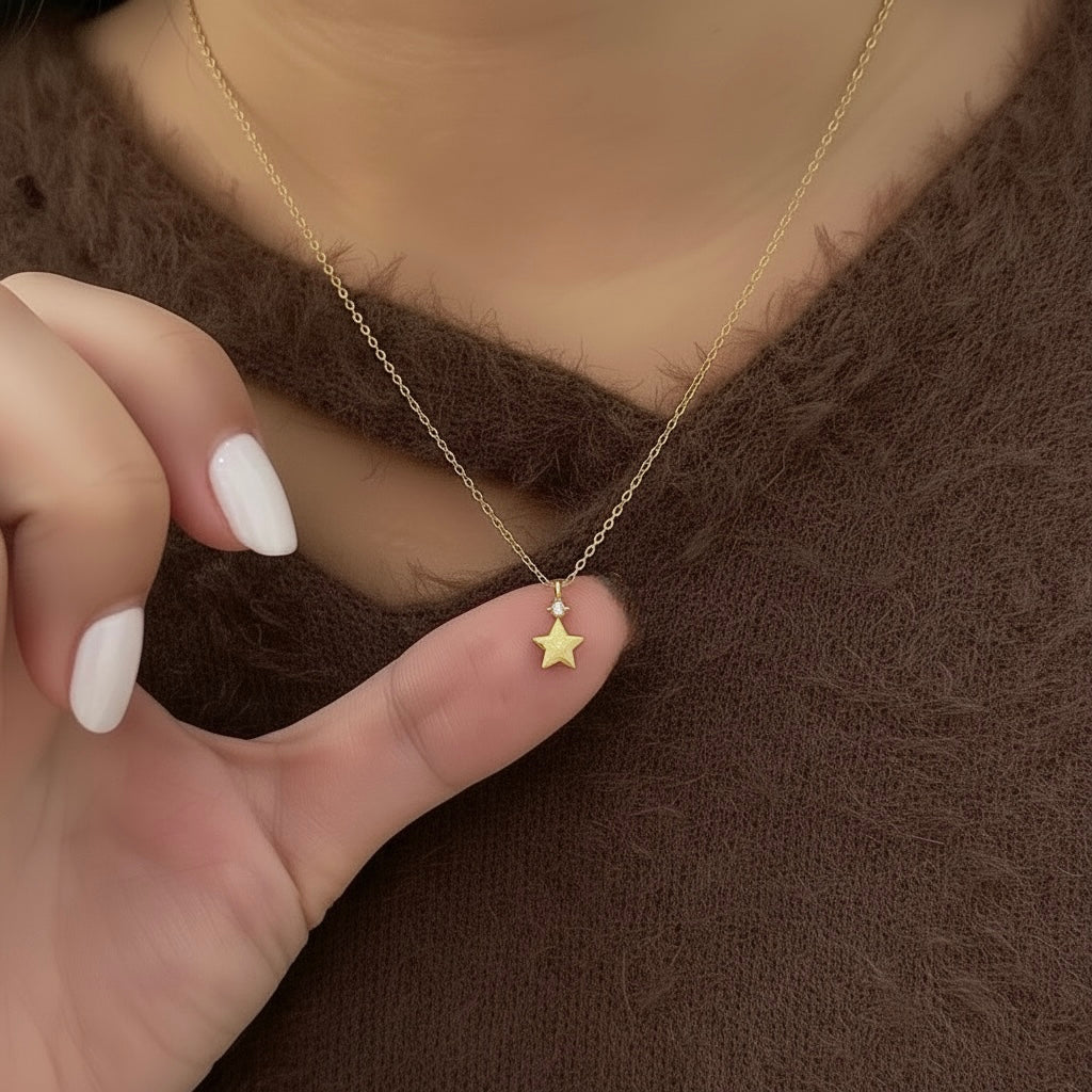 Gold necklace with a star pendant held by a hand against a brown background