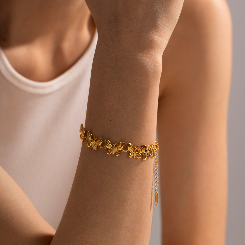 Gold bracelet with leaf designs on a person's wrist against a neutral background