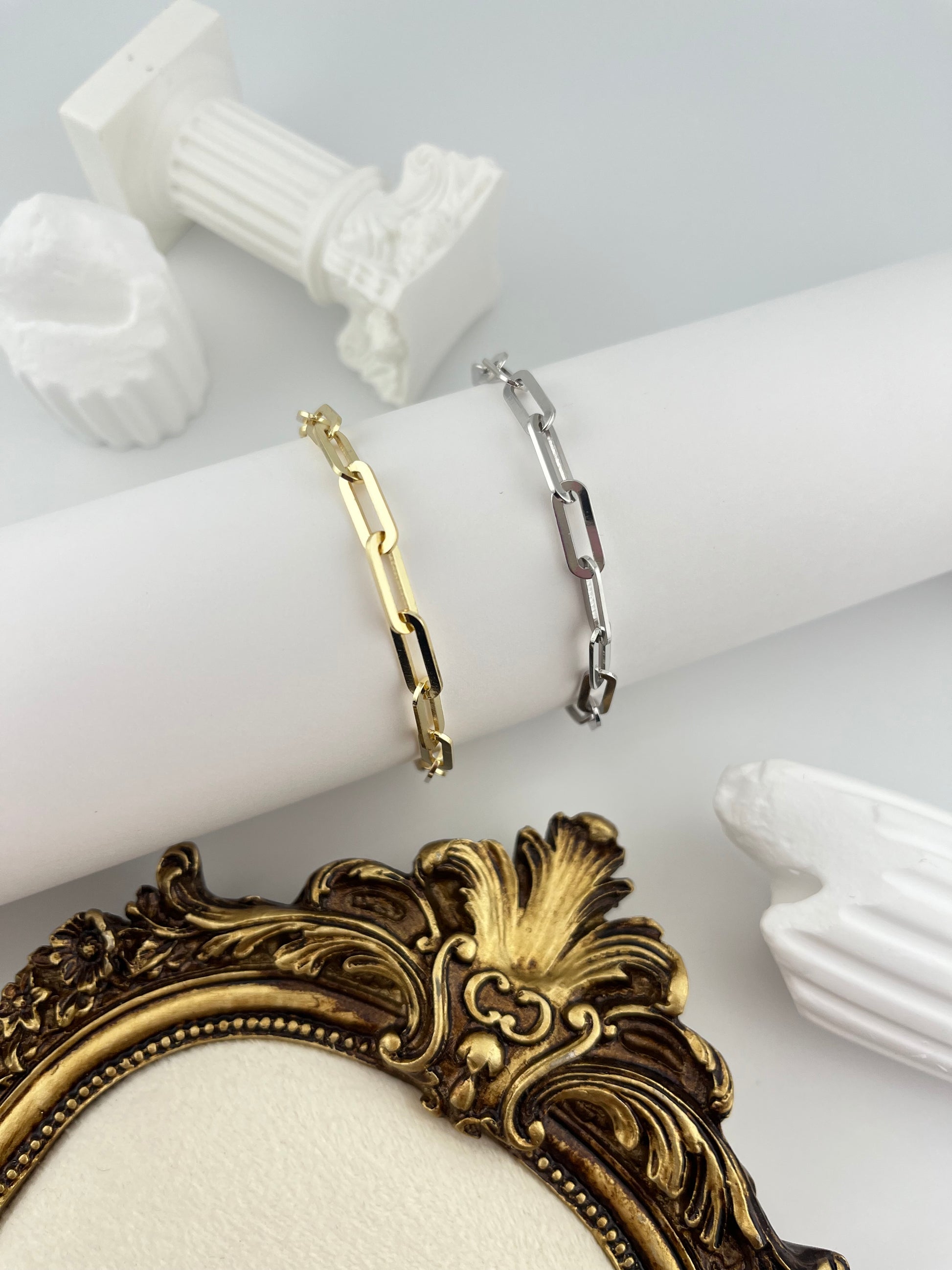 Two bracelets on a white mannequin arm with a decorative gold frame.