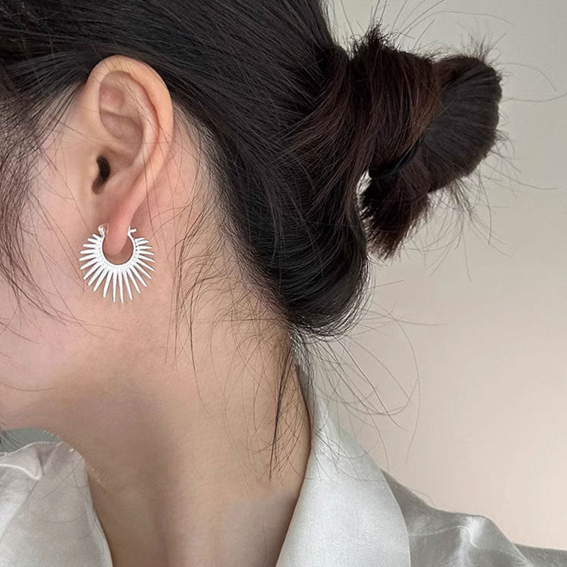Close-up of an ear wearing a silver sunburst earring with a neutral background