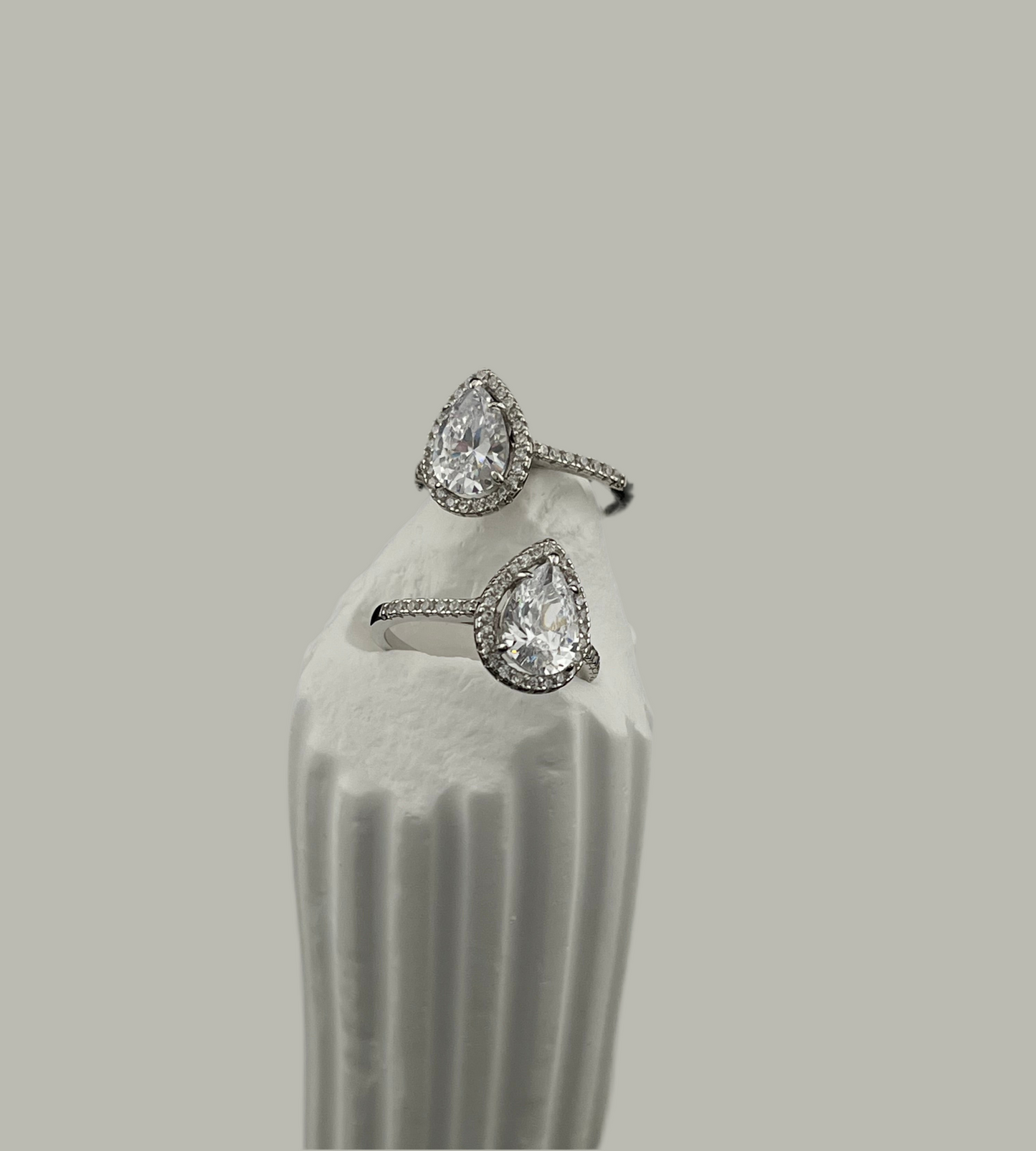 Pair of teardrop-shaped diamond earrings on a white stand against a gray background