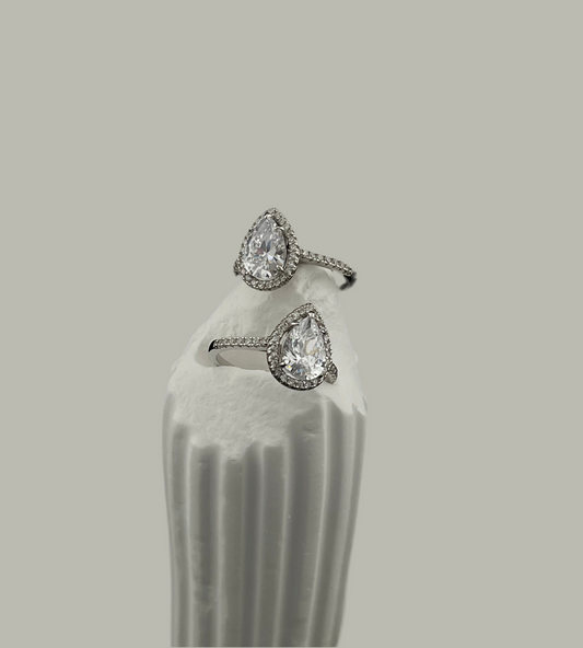 Pair of teardrop-shaped diamond earrings on a white stand against a gray background